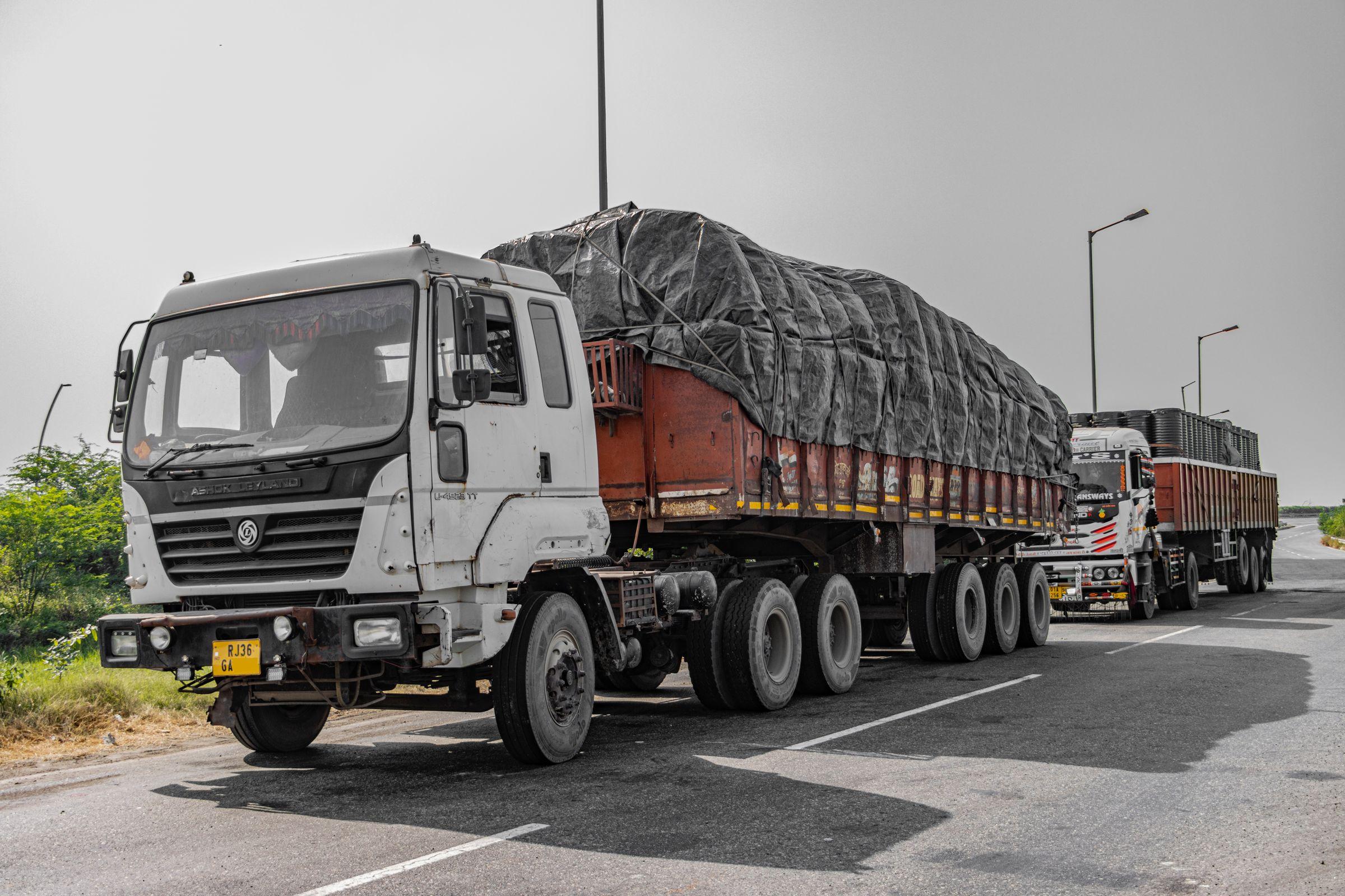 Tractor-trailer goods vehicles with sheeted loads standing at the roadside on an Indian highway
