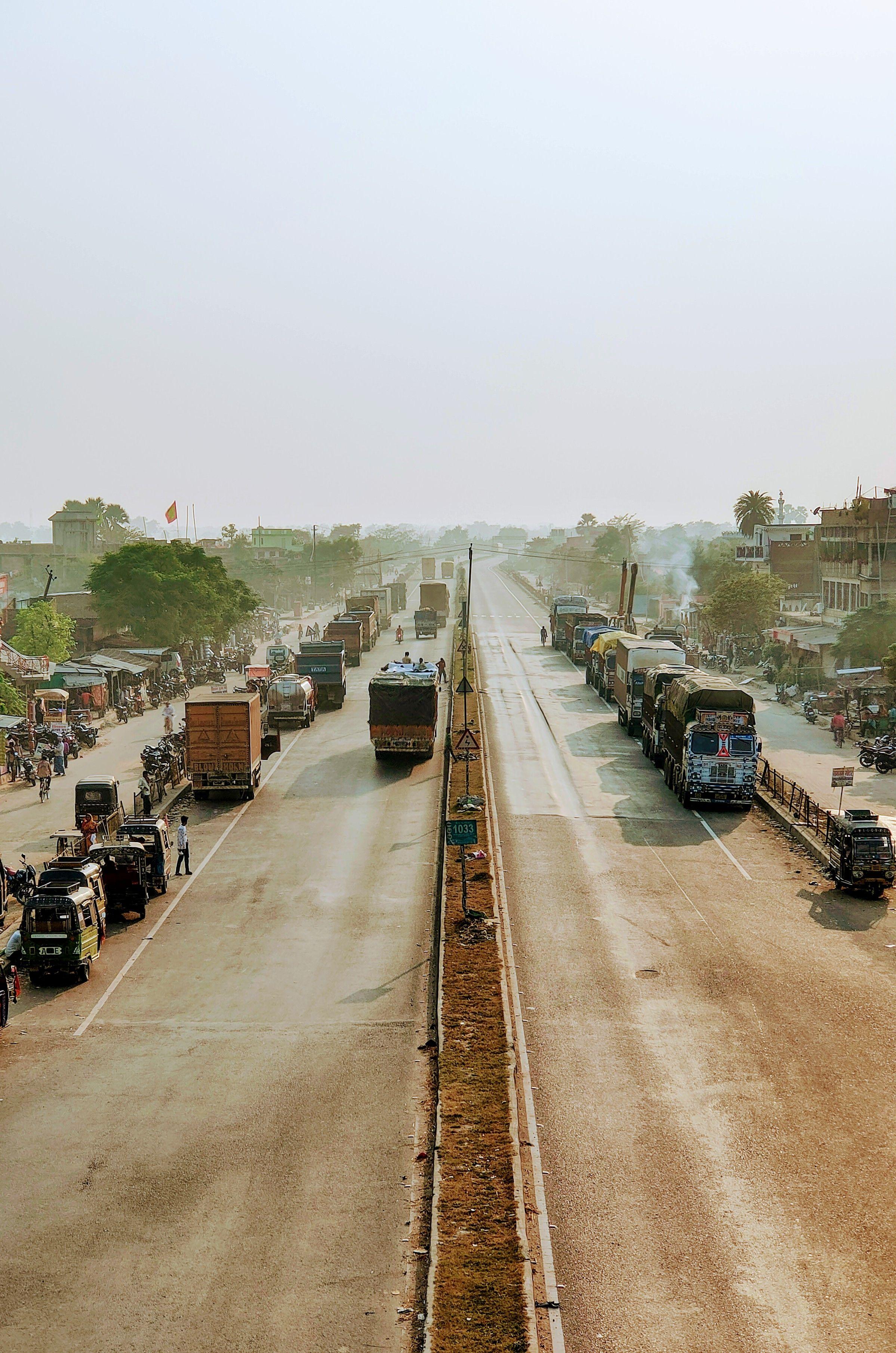 Goods vehicles lining a divided national highway through a roadside town in northern India